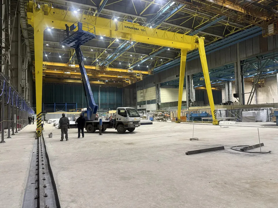 Козловой кран в цехе рядом с автомобильным краном и наземными путями